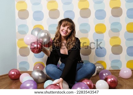 Young Woman Sitting and Holding, Collecting Balloons in Hand Against Colorful Background