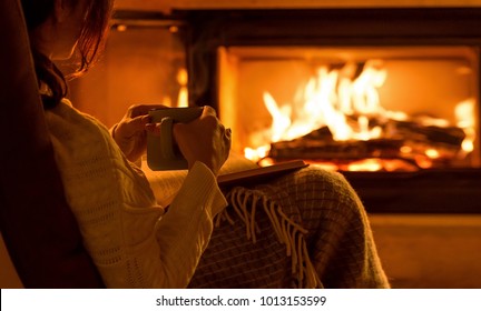 Young woman  sitting at home by the fireplace and reading a book.