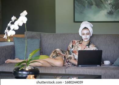 Young Woman Sitting At Home With Face Beauty Mask In Front Of Her Laptop. Cozy Time At Home. Self Time And Home Spa Concept. Coronavirus Outbreak And Self-quarantining Concept.