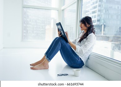 Young woman sitting indoors, by window, on floor using digital tablet. young adult arabic pretty 20 years old