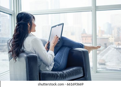 Young woman sitting indoors, in chair using digital tablet, day. young adult arabic pretty 20 years old