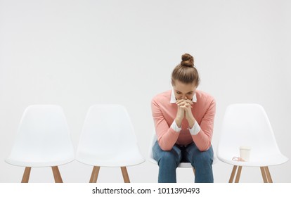 Young Woman Sitting In The Line Or Queue, Looking Stressed, Putting Hands Together As If She Is Praying With Closed Eyes To Overcome Depression