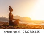 Young woman sitting in lotus pose doing yoga for healthy lifestyle on ocean shore. Woman doing exercises to restore strength and spirit. Yoga pose on sea shore at sunset sea