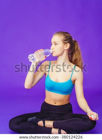 young woman sitting in lotus position with bottle of water on a blue background. Fitness, workout, exercise, drink.