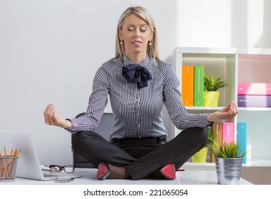 Young Woman Sitting In Lotus Yoga Pose On Desk In Office