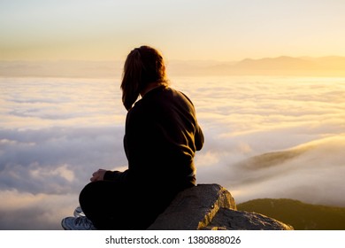 young woman sitting in the mountains over the clouds during sunrise in san diego