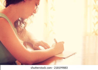 young woman sitting near window and writing. retro filtered image. photograph with natural window light 