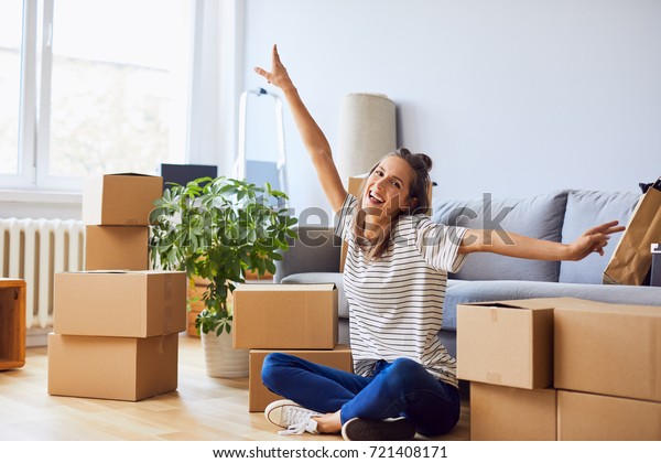 Young woman sitting in new apartment and raising arms\
in joy after moving in