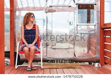 a young woman sitting next to a vintage camper