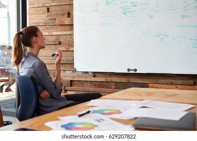 Young Woman Sitting In An Office Reading Notes On Whiteboard