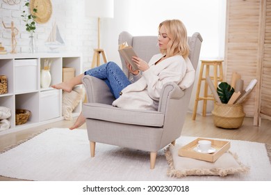 Young Woman Sitting On Armchair And Reading Book At Home