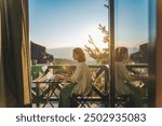 Young woman sitting on balcony with view of mountains and sunset working using laptop