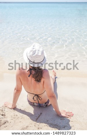 Young woman sitting on a beach looking at clear sea