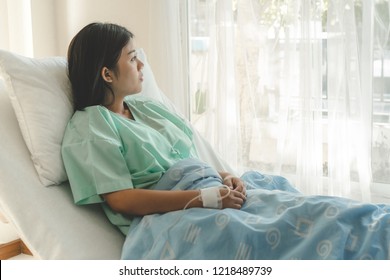 Young Woman Sitting On The Bed And Looking Outside Window In Hospital Worry About Her Illness.