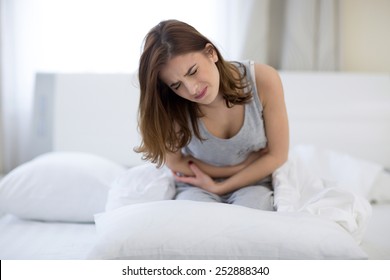 Young Woman Sitting On The Bed With Pain