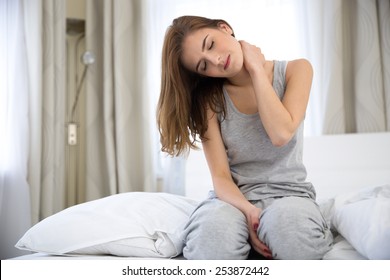 Young Woman Sitting On The Bed With Pain In Neck