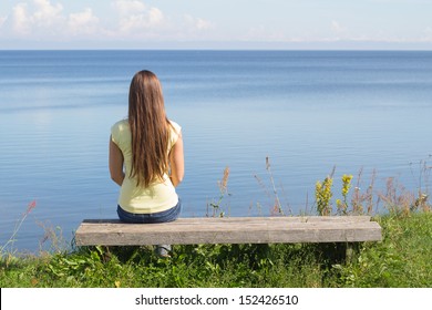 Young woman sitting on bench facing the sea 
