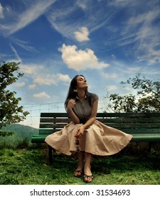 Young Woman Sitting On A Bench In A Park