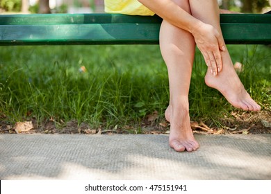 Young Woman Sitting On Bench And Massaging Her Bare Tired Feet