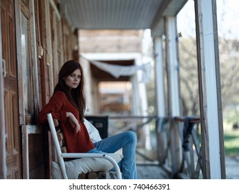young woman sitting on a bench on the veranda near the house, old style