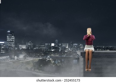 Young Woman Sitting On Building Top And Covering Face With Palms