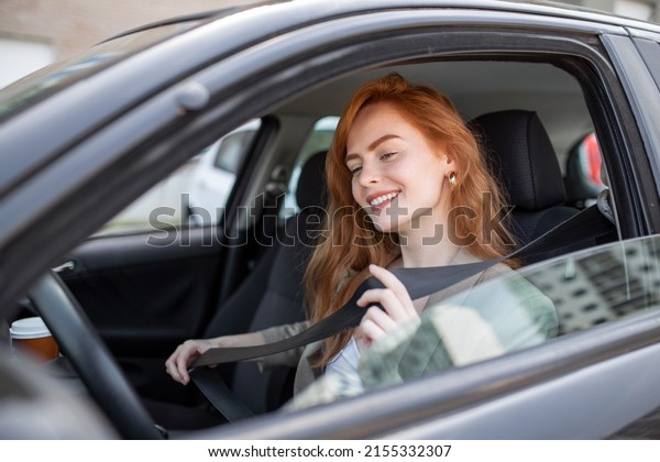 Young woman sitting on car seat and fastening seat belt,\
car safety concept. Woman fastens a seat belt in the car. Caucasian\
woman driver fastening car seat belt while sitting behind the wheel\
