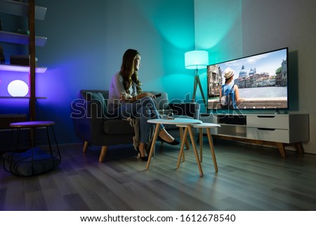 Young Woman Sitting On Carpet Watching Movie On Television At Home