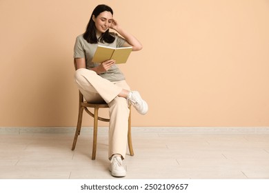 Young woman sitting on chair and reading book near beige wall - Powered by Shutterstock