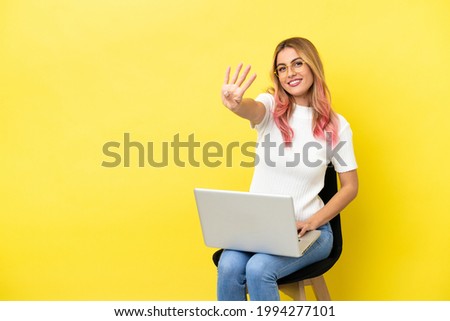 Young woman sitting on a chair with laptop over isolated yellow background happy and counting four with fingers