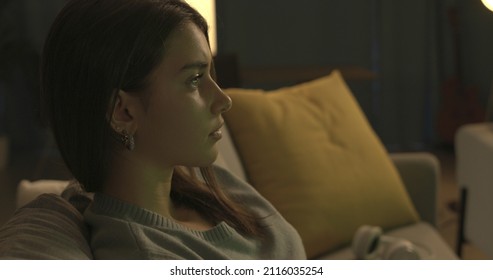 Young Woman Sitting On The Couch And Watching TV At Night, She Is Staring At The Television Screen