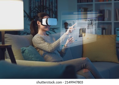 Young woman sitting on the couch and wearing a VR headset, she is interacting with a virtual desktop and browsing the internet - Powered by Shutterstock