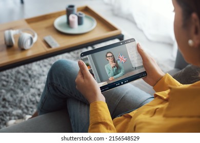 Young woman sitting on the couch at home and connecting with her tablet, she is learning languages online - Powered by Shutterstock