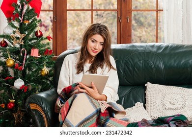  Young Woman Sitting On Couch, Alone, In Front Of Christmas Tree On Living Room,using Tablet Pc.