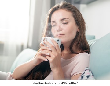 Young woman sitting on couch at home and drinking coffee, casual style indoor shoot