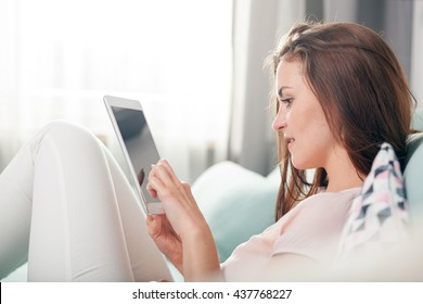 Young Woman Sitting On Couch At Home With Tablet Computer, Casual Style Indoor Shoot