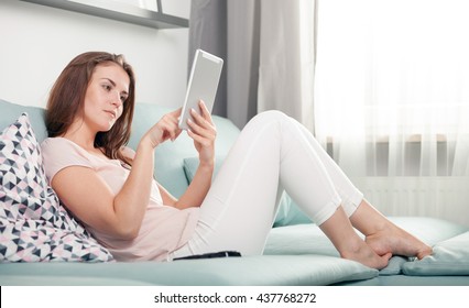 Young Woman Sitting On Couch At Home With Tablet Computer, Casual Style Indoor Shoot