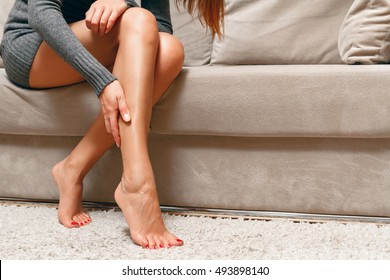 Young woman sitting on the couch suffering from severe pain in the leg