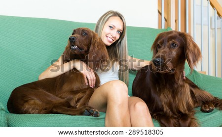 Young woman sitting on a couch with two red Irish setters. Focus on dogs