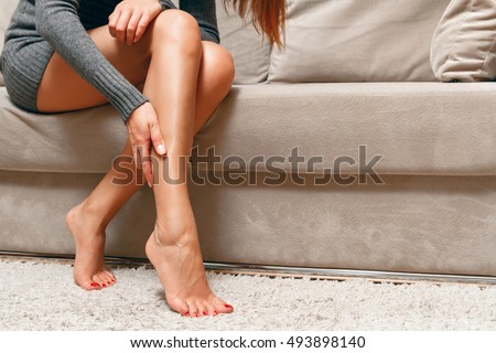 Young woman sitting on the couch suffering from severe pain in the leg