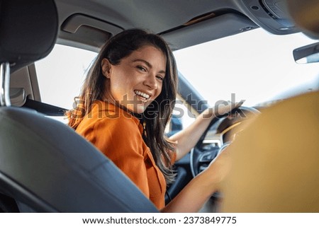 Young woman sitting on a driver's seat in the car and looking at camera over the shoulder. Portrait of pleasant female with positive expression, being satisfied with unforgettable journey by car.