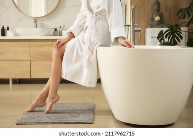 Young woman sitting on edge of tub in bathroom, closeup