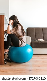 A Young Woman Is Sitting On An Exercise Ball At Her Home And Trying To Work.