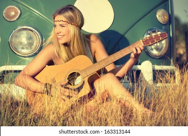 young woman sitting on a field and playing guitar
