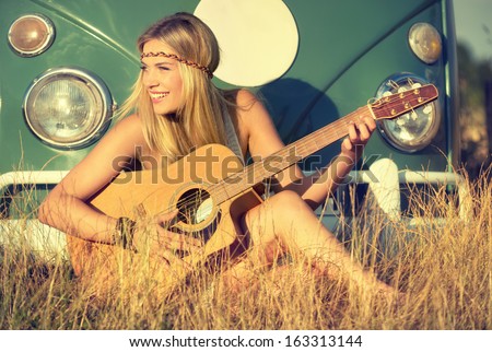 young woman sitting on a field and playing guitar