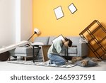 Young woman sitting on floor in living room with messed furniture after earthquake