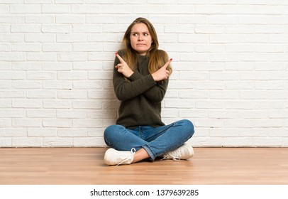 Young woman sitting on the floor pointing to the laterals having doubts - Shutterstock ID 1379639285