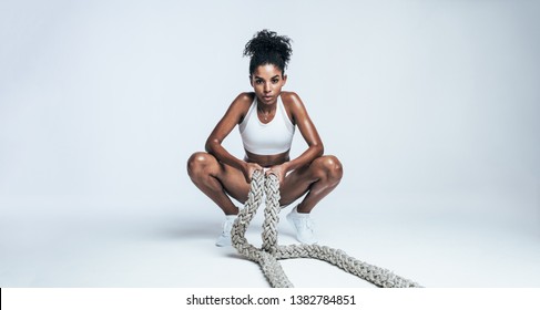 Young woman sitting on floor with battle ropes on white background. Athlete taking rest from intense workout.