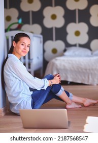 Young Woman Sitting On The Floor Near Children's Cot With Laptop. Young Mom