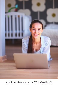 Young Woman Sitting On The Floor Near Children's Cot With Laptop. Young Mom