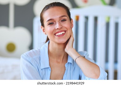 Young Woman Sitting On The Floor Near Children's Cot. Young Mom.